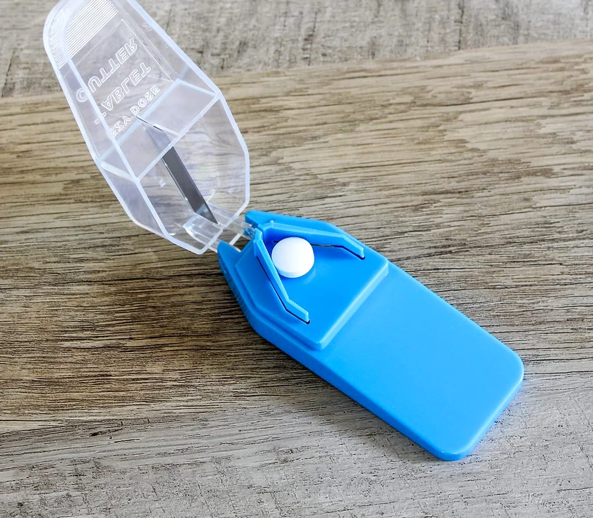 An Ezy Dose pill cutter with safety shield, open, with a tablet in the cradle